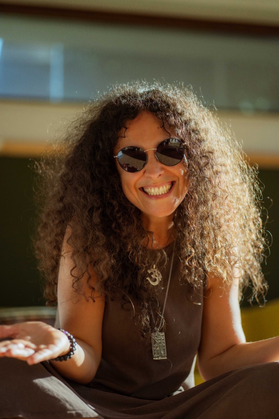 Andrea sitting cross-legged in warm sunlight, laughing with her hands open