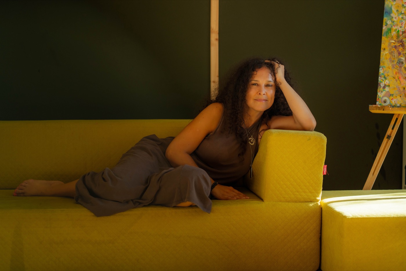 Andrea Varadi Goia reclining on a mustard sofa, head resting on her hand