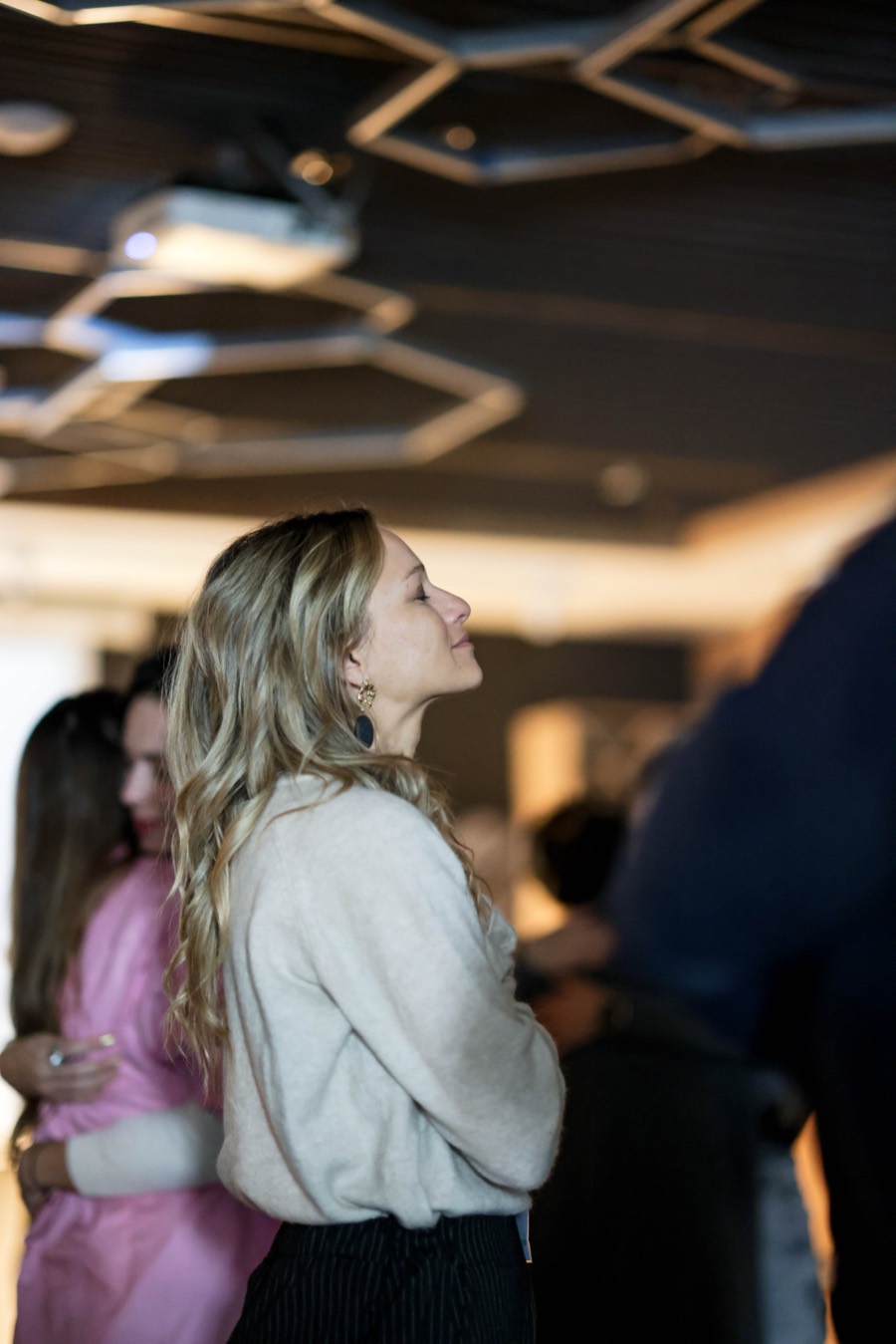 A participant standing in the room, listening, as others embrace behind her