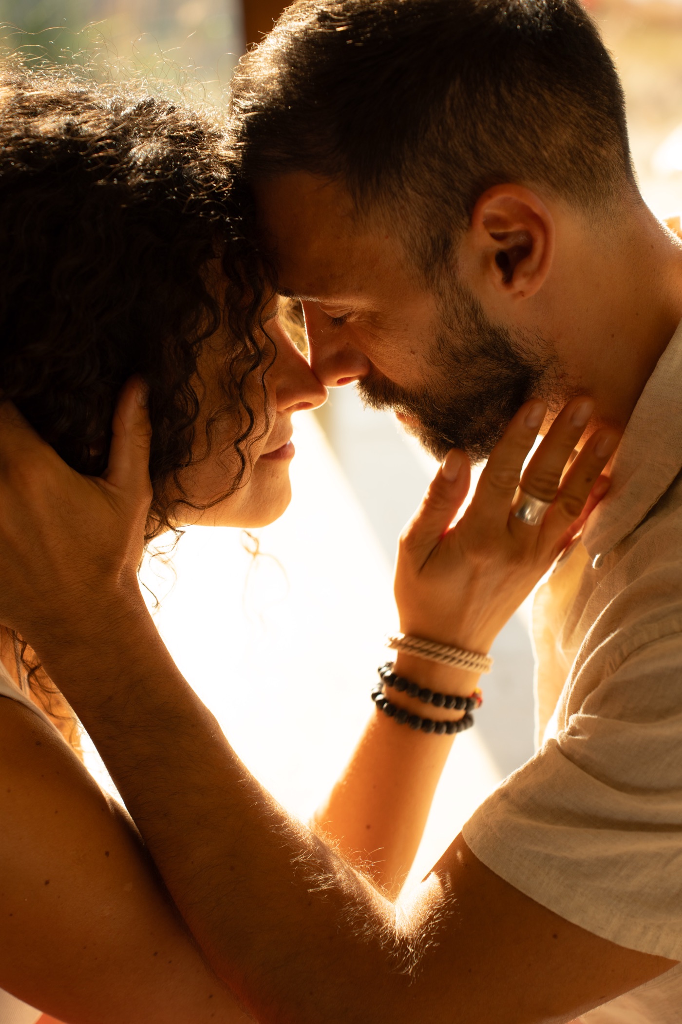 A couple standing forehead to forehead, each holding the other's face, backlit by warm afternoon light