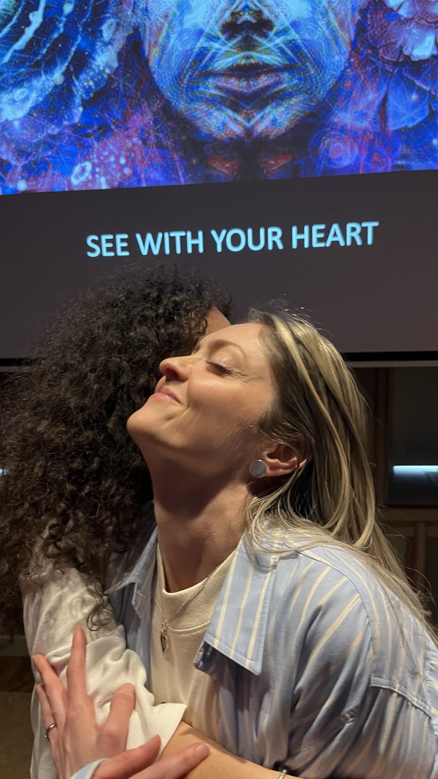 Two participants embracing in front of the See With Your Heart screen