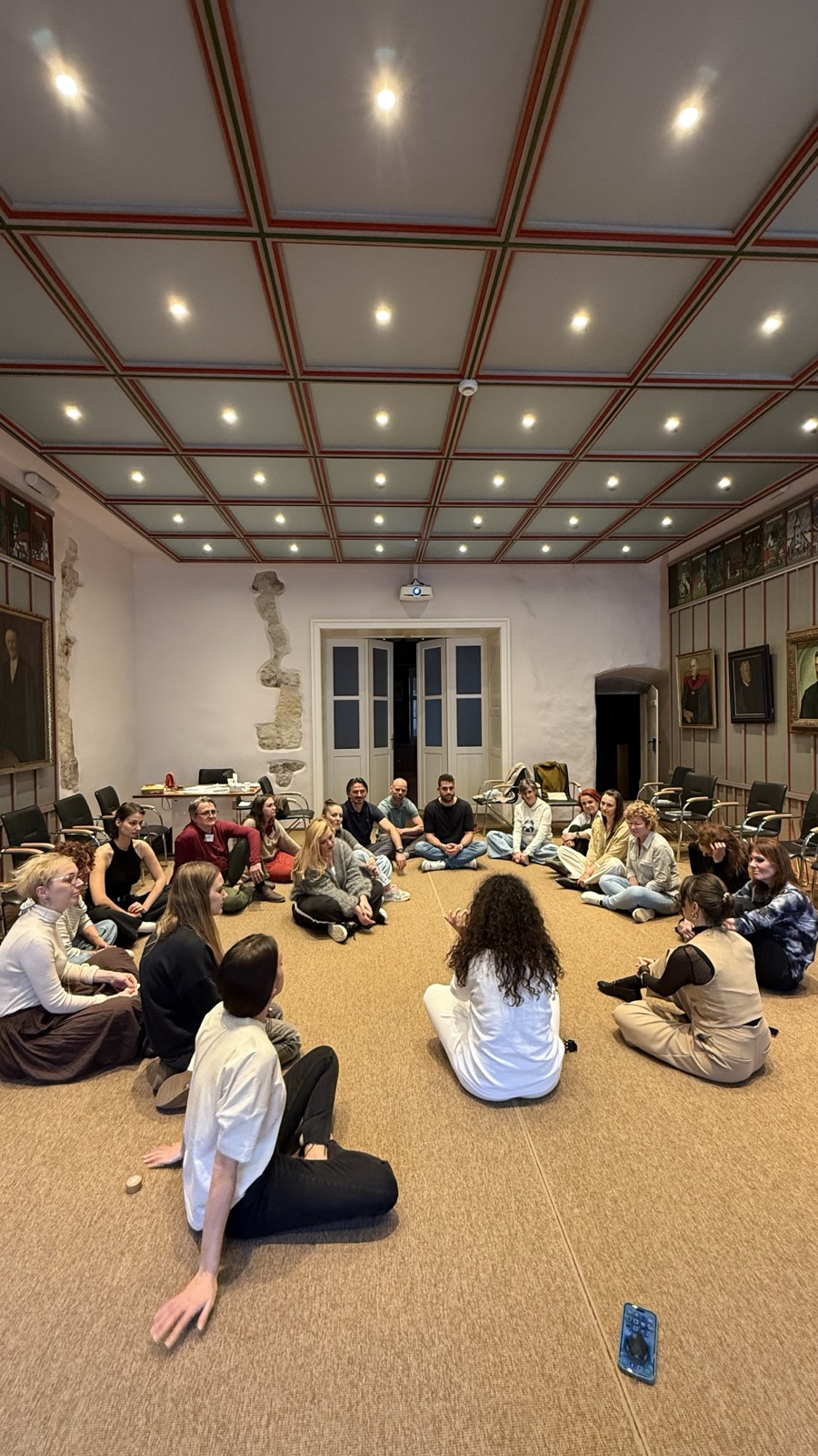 The group seated on the floor in a wide circle in the hall